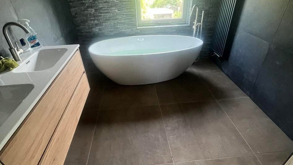 Badkamer met vrijstaand bad, houten wastafelmeubel en donkere vloertegels